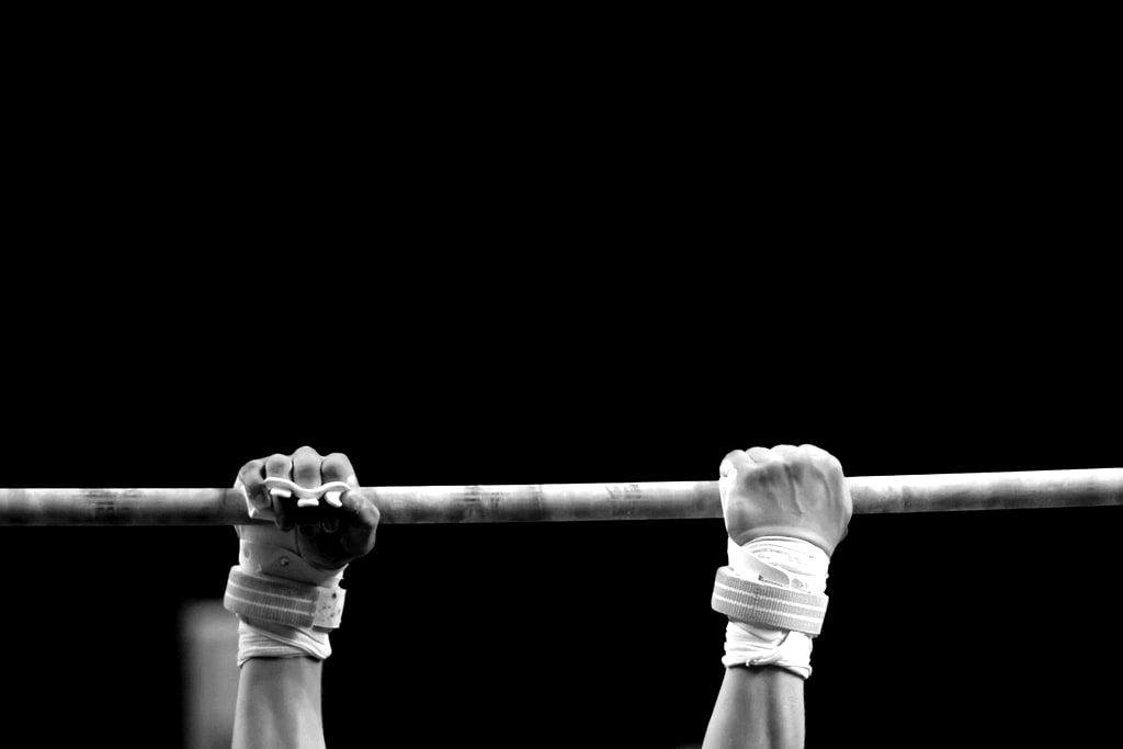 Two taped hands gripping a steel bar against a black background